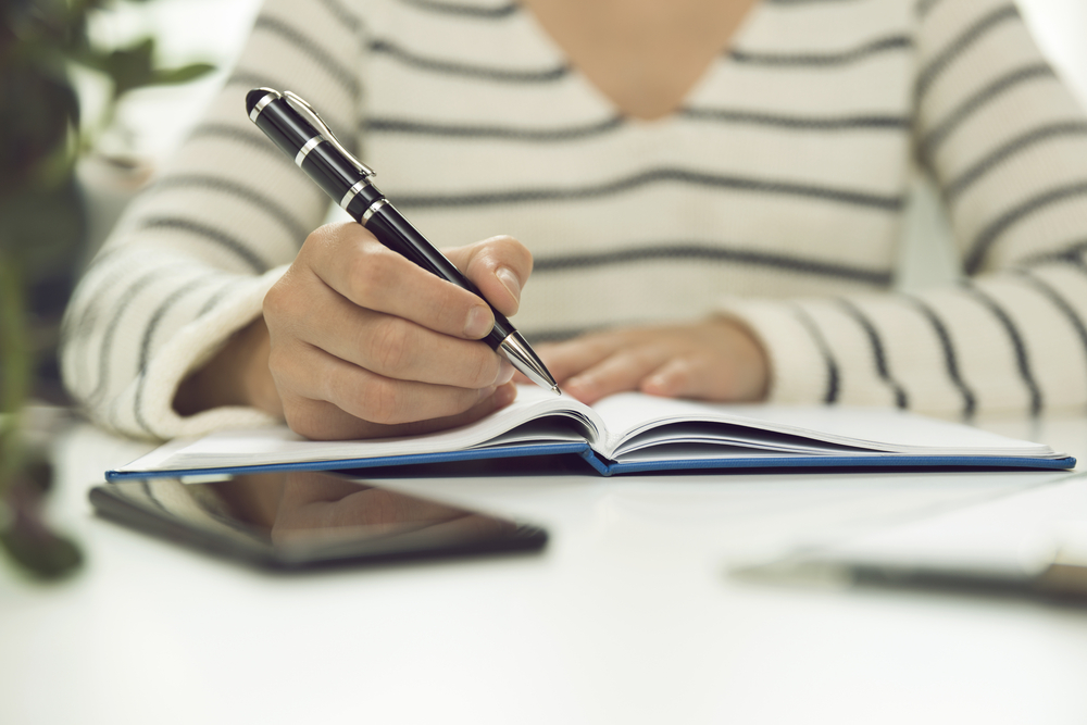 Young woman sitting at table and writing in notebook. 